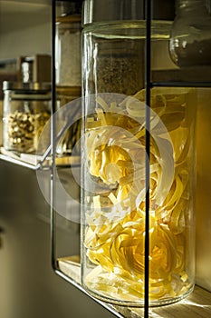 Shelf with seasonings and pastes in large jars in glass close-up on a kitchen wall