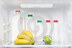 On the shelf of a white fridge, green apple, bananas, body measurement tape and dairy products, kefir, cream, yogurt