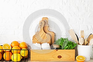 Shelf in a white kitchen with fresh fruits, herbs, cutlery, kitchen utensils, tools, textiles, fresh water in a decanter