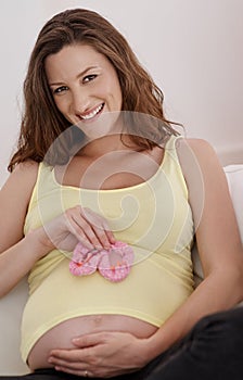 Shell look adorable in this. a young pregnant woman holding a pair of pink baby shoes against her belly.