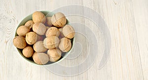 In-shell walnuts are poured into a cup on a light-colored wooden surface