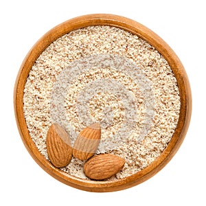 Shelled and ground almond nuts in wooden bowl over white