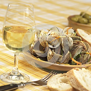 shells in white-wine sauce and root vegetables served glass of white wine bread slices and olives