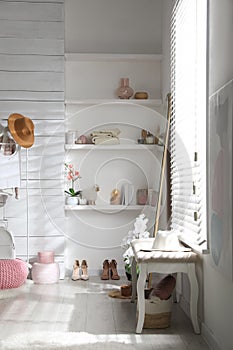 Shelves with different decorative elements, shoes and  bench in dressing room. Interior design