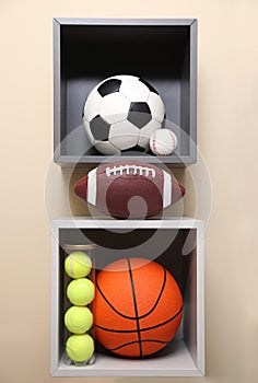 Shelves with different sport balls on beige wall indoors