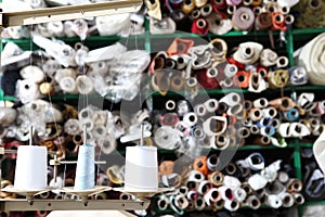 Shelves with rolls of colored fabrics and spools of sewing thread in the foreground