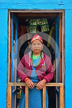 Nepalese Sherpa woman in traditional attire standing at front blue door along Everest Base Camp village, Nepal