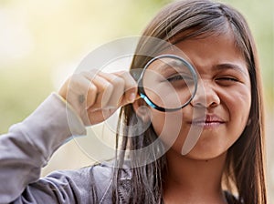 Shes on another one of her explorations. Portrait of a little girl looking through a magnifying glass.