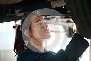 Shes the best auto mechanic there is. a female mechanic working under a lifted car.