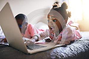 Shes a bundle of excitement. an adorable little girl playing on a laptop next to her brother at home.