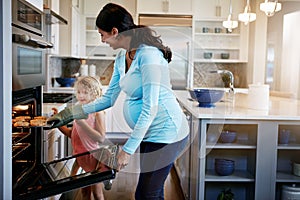 Shes eager to try one. a little girl watching her mother take a tray of cookies out of the oven.