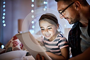 Shes excited to pick the story. a father reading his young daughter a bedtime story on a tablet.