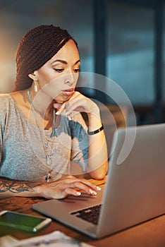 Shes focused on meeting her deadlines. a young woman using her laptop while working late in her office.