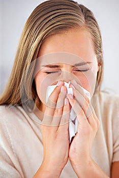 Shes getting the sniffles. a young woman blowing her nose into a tissue.
