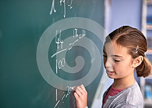 Shes almost got it. an elementary school girl writing on a blackboard in class.