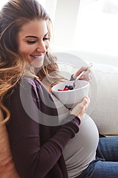 Shes got that glow. an attractive young pregnant woman eating breakfast while sitting on the sofa at home.