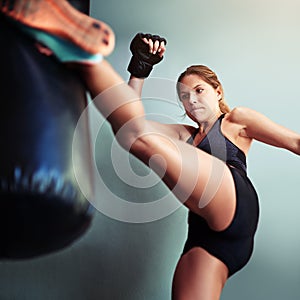 Shes got a lot of fight in her. Shot of a female boxer kicking a punching bag.