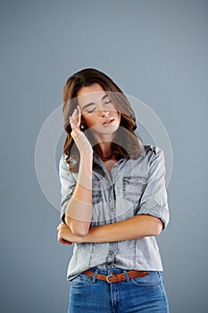 Shes got a serious migraine. Studio shot of an attractive young woman suffering with a headache against a grey