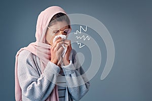 Shes got the sniffles. Studio shot of an attractive young woman blowing her nose while standing against a grey