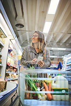 Shes got the ultimate shopping list on her phone. a young woman using a mobile phone in a grocery store.