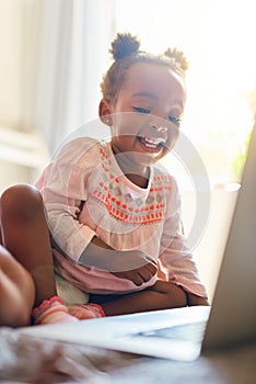 Shes having a whale of a time. an adorable little girl using a laptop at home.