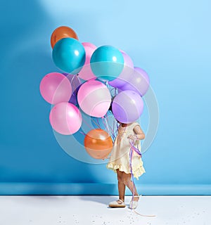 Shes a hidden cutey. a cute little girl standing behind a bunch of balloons.