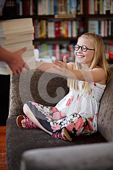 Shes a little bookworm. A cute little blonde girl smiling as someone brings her a stack of books in a library.