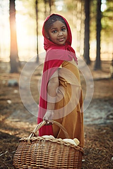 Shes a little red riding hood. Portrait of a little girl dressed in a red cape and holding a basket in the woods.