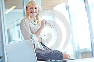Shes a model employee. Portrait of a smiling business woman sitting on her desk with her laptop in front of her with