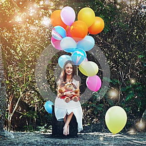 Shes one carefree kid with a big imagination. Portrait of a little girl playing with a teddybear and bunch of balloons