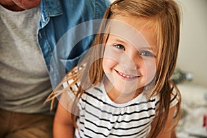 Shes such a cute little one. Portrait of a smiling little girl sitting with her father at home.