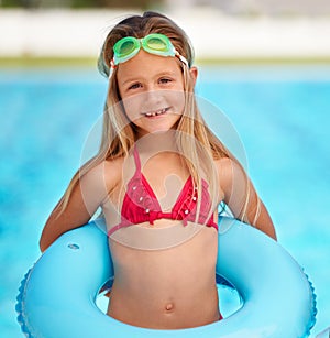 Shes a Summer child. A cute little girl using a pool inflatable while swimming.