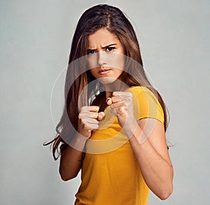 Shes a really tough cookie. Studio portrait of an attractive woman putting up her firsts against a grey background.