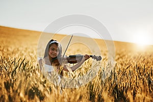 Shes in tune with nature. Portrait of a cute little girl playing the violin while standing in a cornfield.