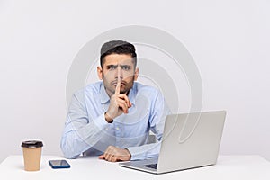 Shh, be quiet! Businessman sitting office workplace with laptop on desk, asking for silence or secrecy
