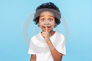 Shh, be quiet! Portrait of funny cute little boy with curly hair in T-shirt making silence gesture with finger on his lips photo