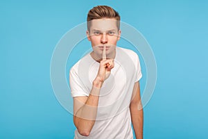 Shh, be quiet! Portrait of serious man in casual white t-shirt shushing to camera with finger on lips