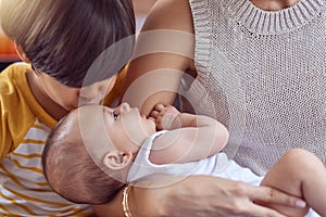 Shh, big brother is here. an adorable little boy kissing his baby brother while his mother cradles him at home.