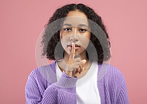 Shh, keep silence, confidential information. Young African American woman gesturing hush on pink studio background