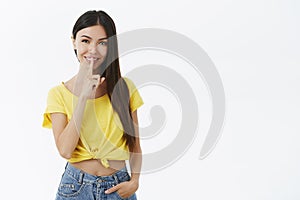 Shh keep it between us. Charming mysterious and flirty young woman in trendy yellow t-shirt making shush gesture with photo