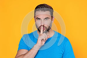 Shh man. Portrait of man showing shh taboo sign with finger to lips over yellow studio background. The secret. Hush shut