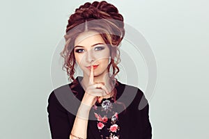 Shh. Woman asking for silence or secrecy with finger on lips hush hand gesture light green background wall. Pretty girl placing