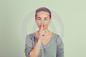 SHH. Woman wide eyed asking for silence or secrecy with finger on lips hush hand gesture green background wall. Pretty girl