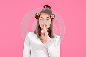 Shh, womens secrets. Woman with curlers showing secret sign. Funny housewife. Closeup portrait of young woman is showing