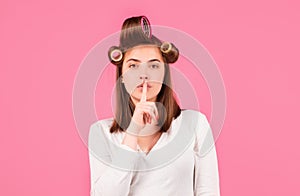 Shh, womens secrets. Woman with curlers showing secret sign. Funny housewife. Closeup portrait of young woman is showing