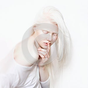 Shhh gesture. Albino female with white skin and white long hair. Photo face on a light background. Blonde girl photo