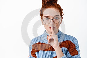 Shhh its a secret. Cute redhead hipster girl shushing, asking to be quiet or stay silent, making taboo gesture, standing