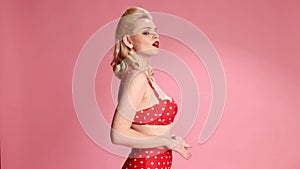 Shhh. Secrets. Beautiful young blonde girl with retro hairstyle in swimming suit over pink studio background. Pin-up