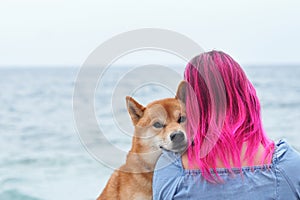 A Shiba Inu dog cozily nestles into a woman with striking pink hair