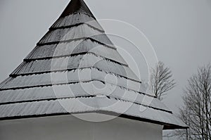 Shingled wooden roof on a building in the mountains. snow and icing covered in chipped shingles. brown, black and white are very t